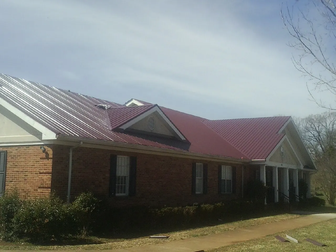 Red metal roof with gabled entries on a long brick building, from a Hail Damage Roof Repair job in Gales Ferry