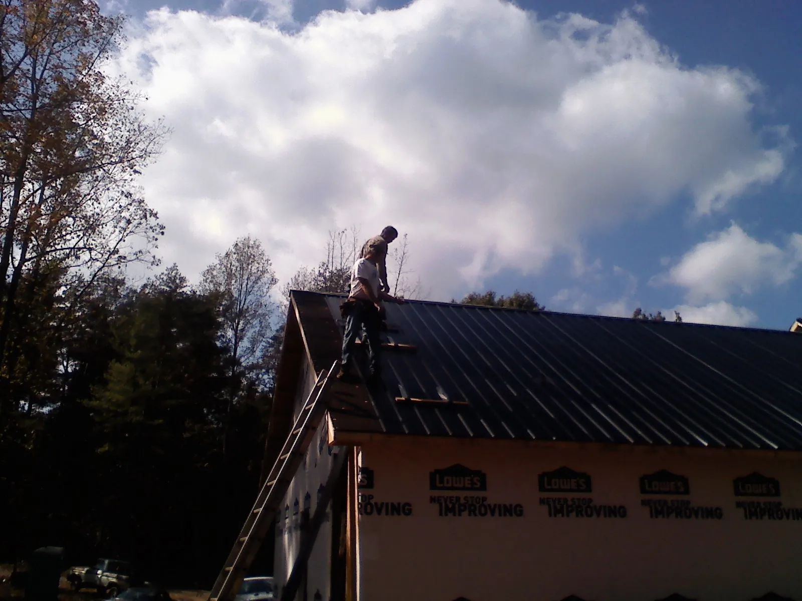 Roofer fastening dark metal panels high against a cloudy sky, from a Roof Inspection job in Gales Ferry