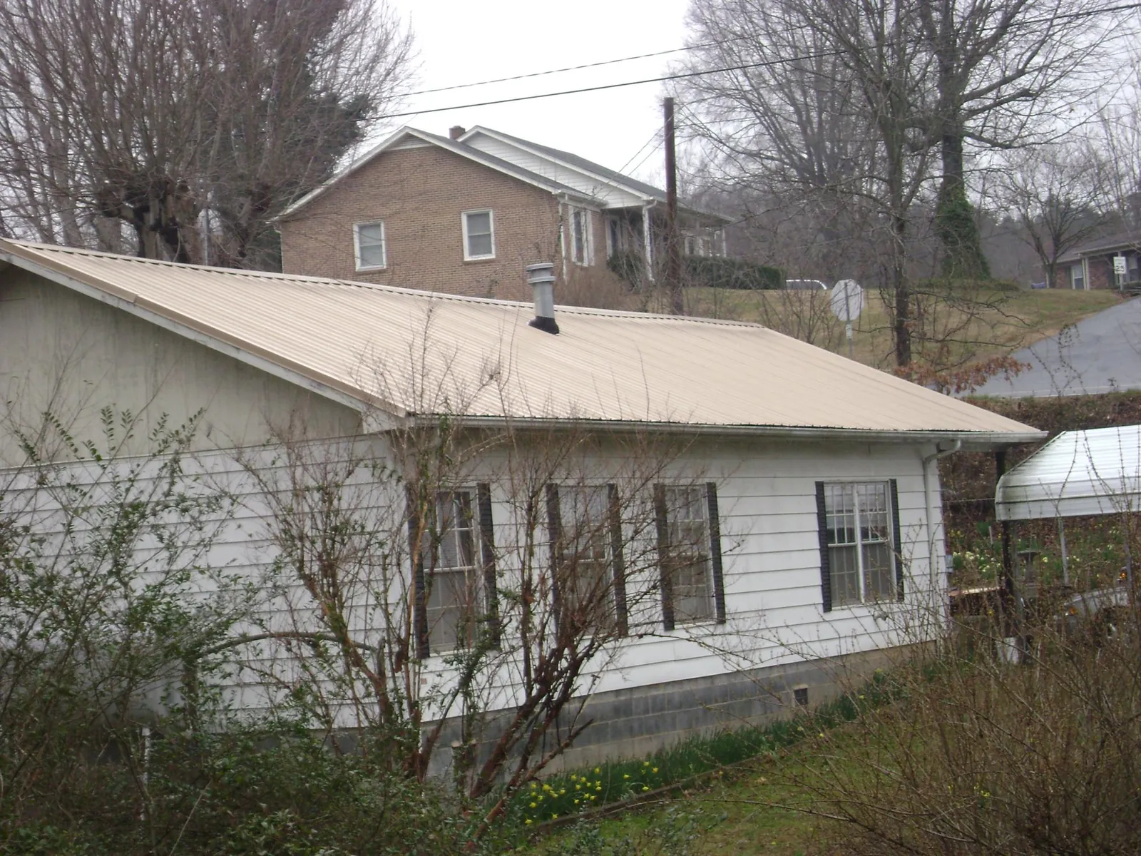 Tan metal roof on a white sided house set into a hillside — Commercial Roofing by Roofing Brothers in Gales Ferry